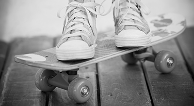 Feet in sneakers on a skateboard situated on a wooden balcony (black and white)