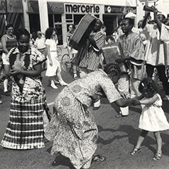 A woman and a little girl are dancing. Next to them, another woman is also dancing. Men are playing music with instruments.