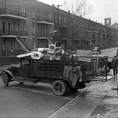 Moving scene where a truck is loaded with furniture, mattresses and chairs. A man is standing on the load.