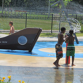 Quatre enfants jouent dans des jeux d’eau extérieurs.