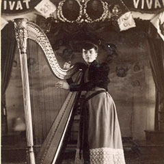 A young woman, Nellie Madigan, poses next to a harp.