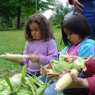 Deux fillettes, aux traits latino-américains, épluchent des épis de maïs dans un parc.
